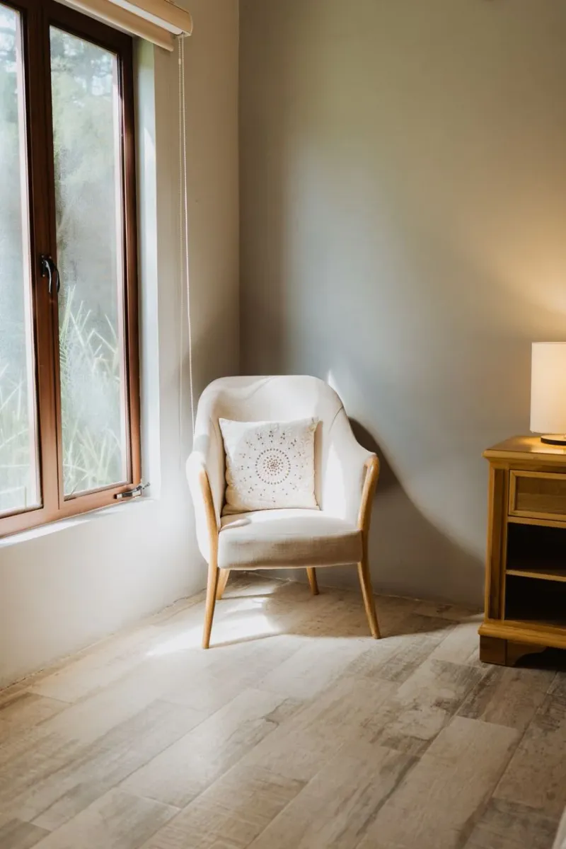 A sunlit white armchair by a window in a calm minimal interior